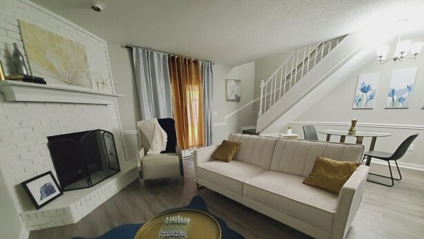 Ein Wohnzimmer mit weißem Sofa, einem runden Couchtisch, einem Kamin und einer Treppe, die zu einer anderen Ebene führt.