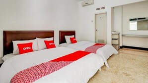 A hotel room with two beds, each with a wooden headboard, white bedding, and red pillows. There is a small bedside table with a lamp, a window with blinds, and an air conditioning unit on the wall. - OYO 3341 Ten Guest House (Bandung)