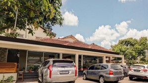 A modern building with a tiled roof, a covered entrance, and several parked cars. - OYO 3341 Ten Guest House (Bandung)