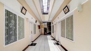 A hotel corridor with a tiled floor, large windows with bamboo designs, and framed pictures on the walls. - OYO 3341 Ten Guest House (Bandung)