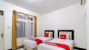 A hotel room with two beds, each with a red and white bedspread, and a window with sheer curtains. - OYO 3341 Ten Guest House (Bandung)