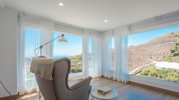 Ein Zimmer mit großem Fenster und Blick auf eine hügelige Landschaft.