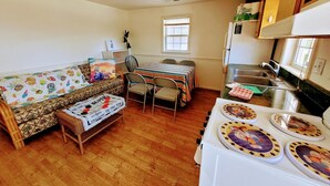 A compact living space with a sofa, a dining table, chairs, a kitchen area with a stove, and a window providing natural light. - SunSplash,  WALK TO THE BEACH, WALK TO MAIN STREET (North Myrtle Beach)