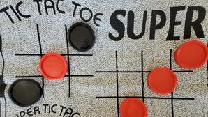A tic-tac-toe game on a textured fabric with black and red tokens. - SunSplash,  WALK TO THE BEACH, WALK TO MAIN STREET (North Myrtle Beach)