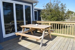 A wooden deck with a picnic table and benches, surrounded by a wooden railing and a house with large windows. - Avocet- Shared Community Water Access, Close to Beach. (Chincoteague)