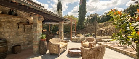 A stone building with a pergola, wicker furniture, and a stone barrel.