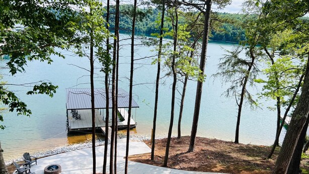 Una cabaña junto al lago con un muelle, rodeada de árboles y un sendero para caminar.