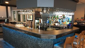 A bar area with a stone-textured counter, bar stools, and a variety of liquor bottles. - Manitou Springs Resort (Manitou Beach)