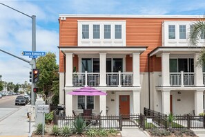 A two-story residential building with a balcony, a street sign, and a parked car.