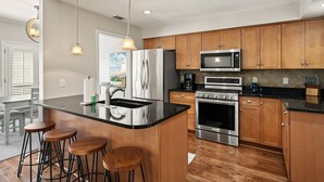 Una cocina moderna con armarios de madera, electrodomésticos de acero inoxidable y una zona de bar con taburetes.