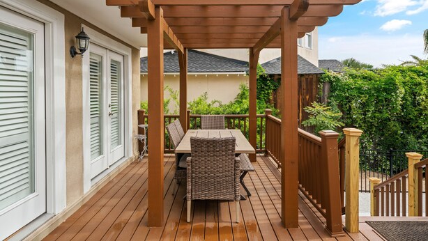 Una terraza de madera con pérgola, una mesa y sillas.