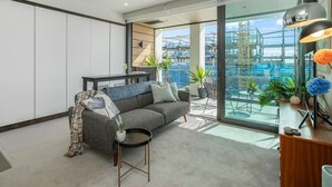 A modern living room with a grey sofa, a small round table, and a view of a construction site through large glass windows.