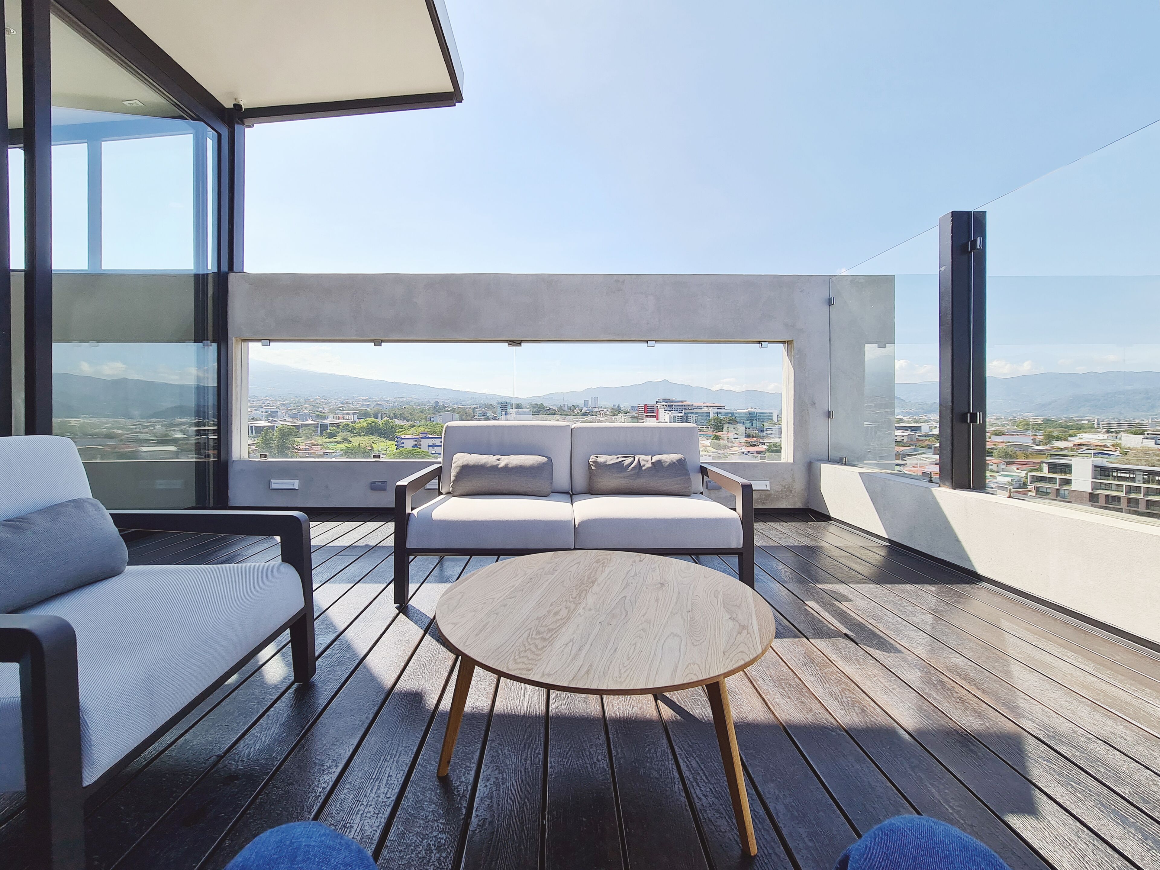 Un balcón con sofá, una mesa redonda y vistas a la ciudad y montañas.