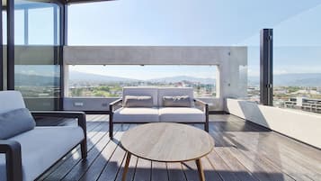 Un balcón con sofá, una mesa redonda y vistas a la ciudad y montañas.