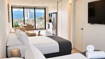 Une chambre d’hôtel avec deux lits, une télévision, un coin repas avec vue et un balcon donnant sur la ville.