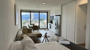 A modern hotel room with a large bed, a seating area with sofas, a dining table, and a kitchen area. - BEE Suites San Jose - Escalante (San José)