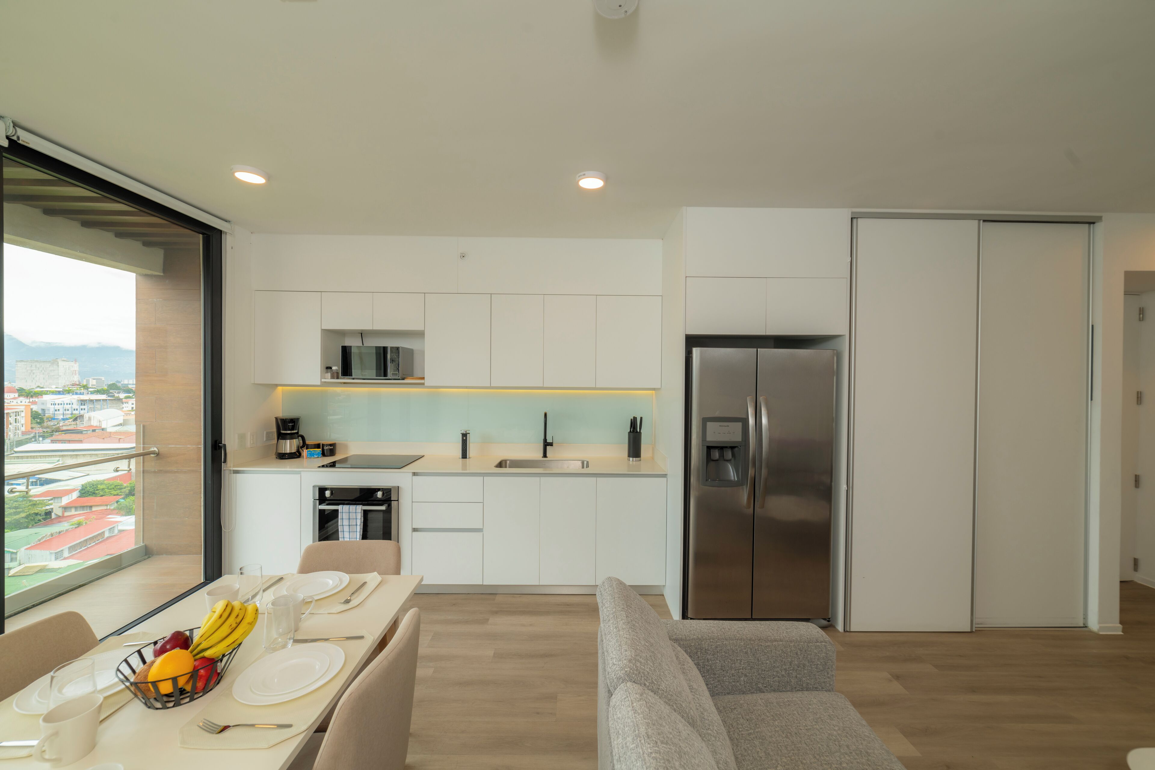 A modern kitchen with white cabinets, a stainless steel refrigerator, and a dining area with a table set for two.