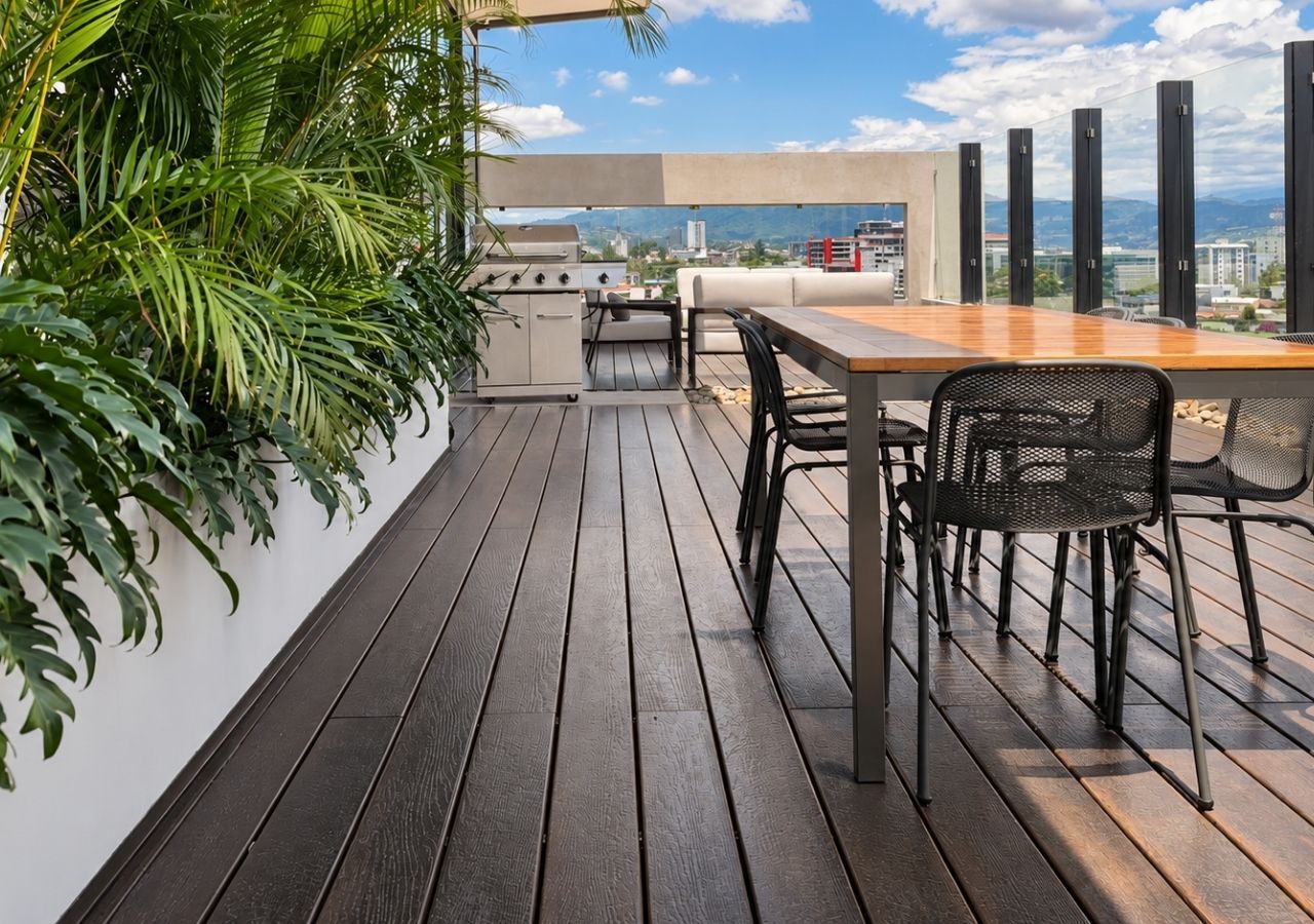Una terraza en la azotea con piso de madera, una parrilla, una mesa de comedor con sillas y vistas a la ciudad.