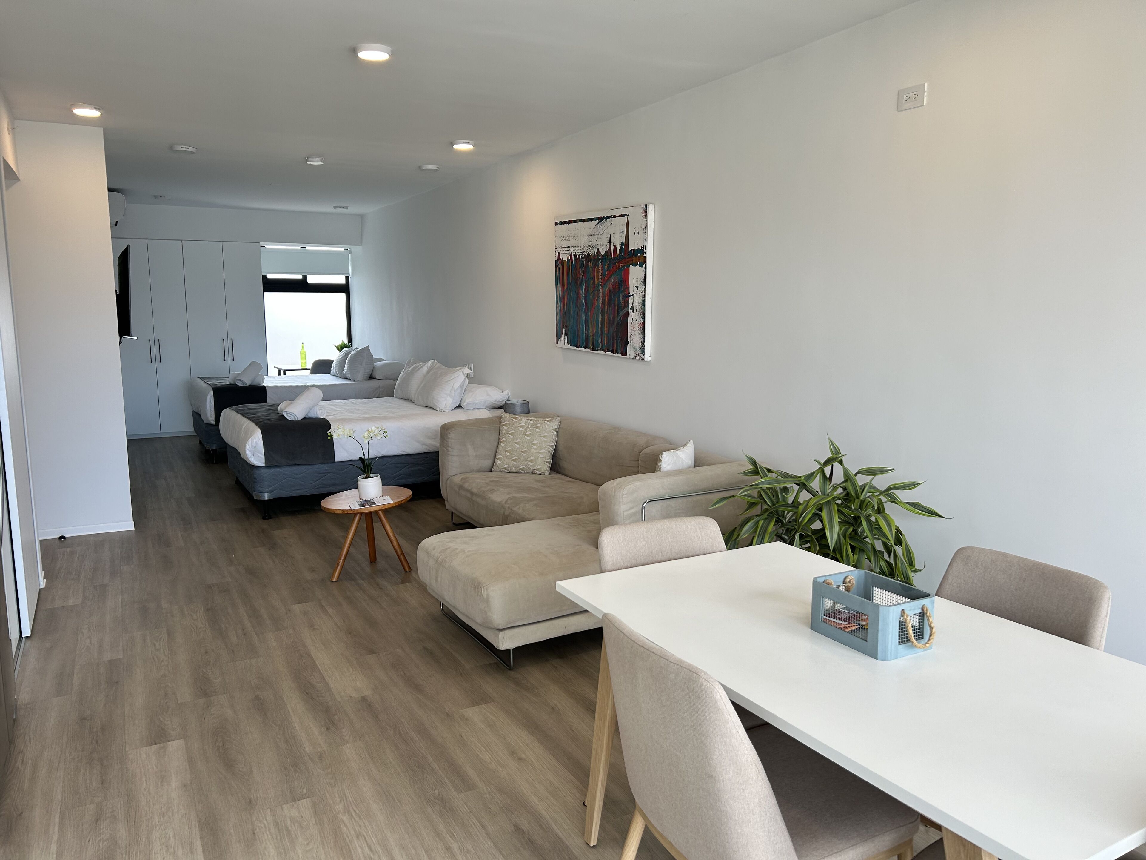 A modern, well-lit room with a bed, a sofa, a dining table, and a small side table.