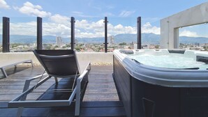 A rooftop terrace with a hot tub and lounge chairs, overlooking a cityscape and mountains. - BEE Suites San Jose - Escalante (San José)