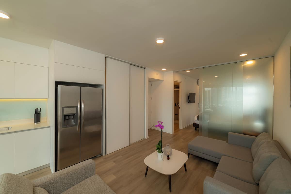 Una sala de estar moderna con un sofá, una mesa de centro, un refrigerador y una zona de cocina.