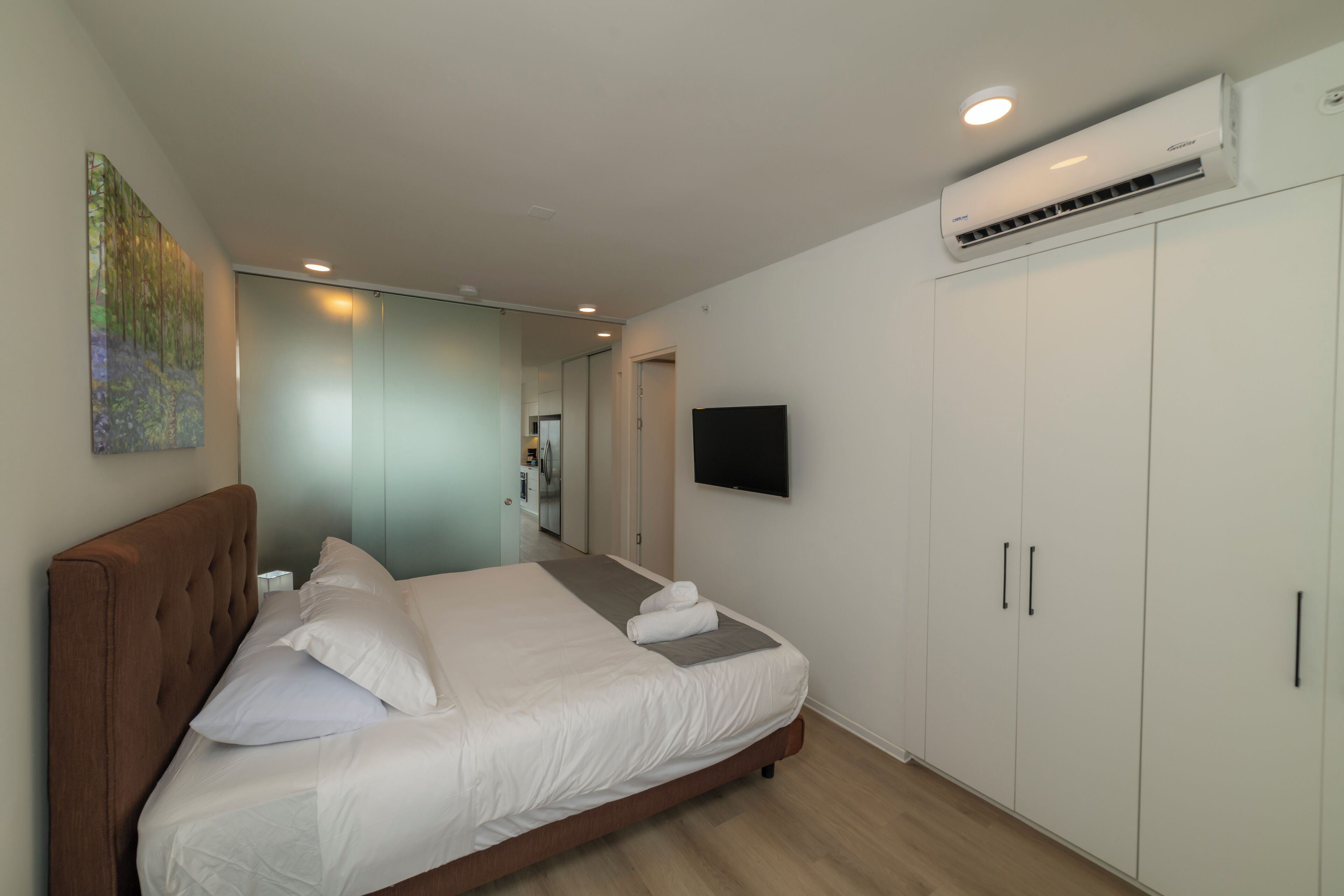 A modern hotel room with a large bed, a flat-screen TV, an air conditioning unit, and a wardrobe.
