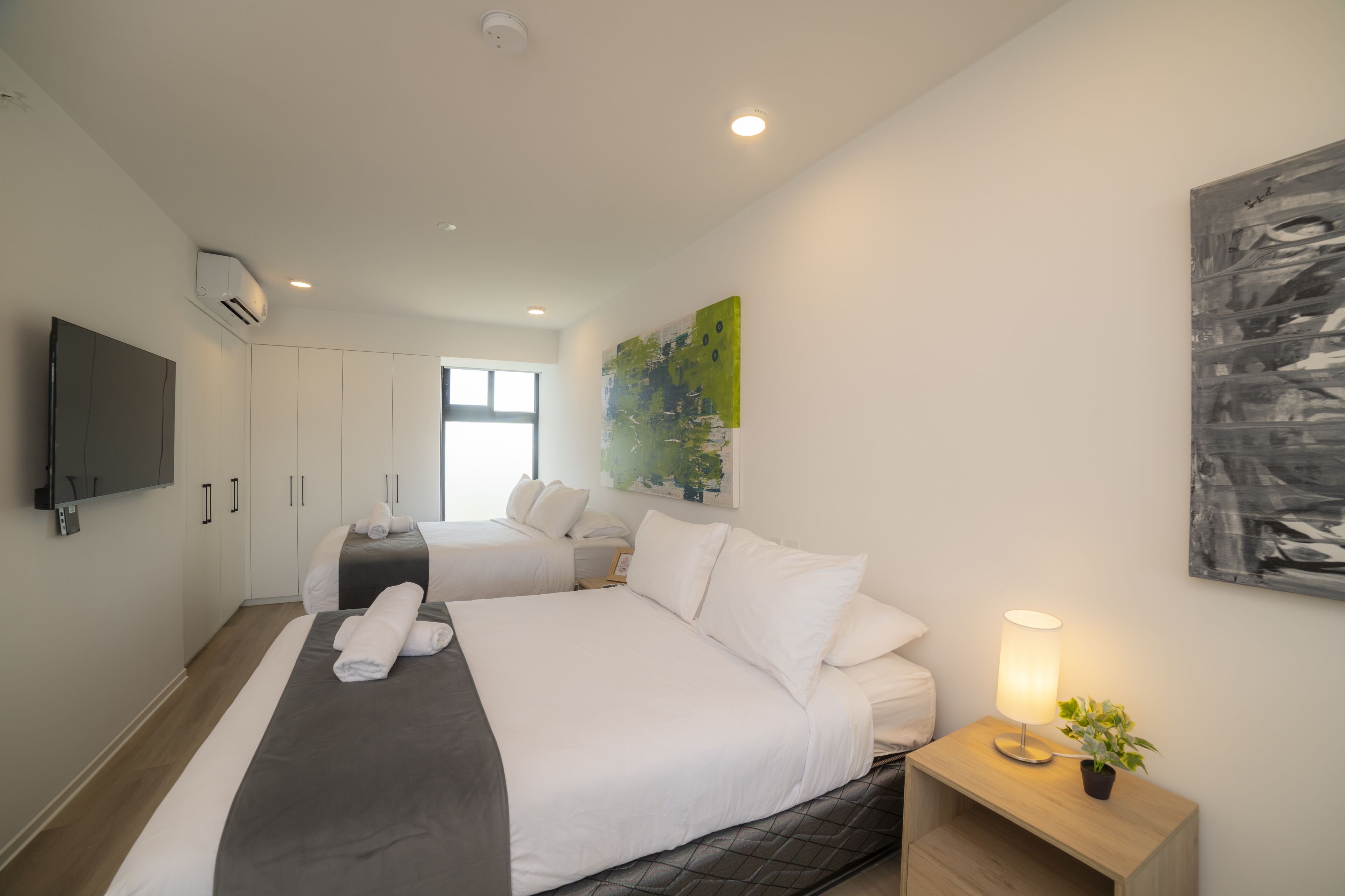 A hotel room with two beds, a TV, a painting, and a lamp.