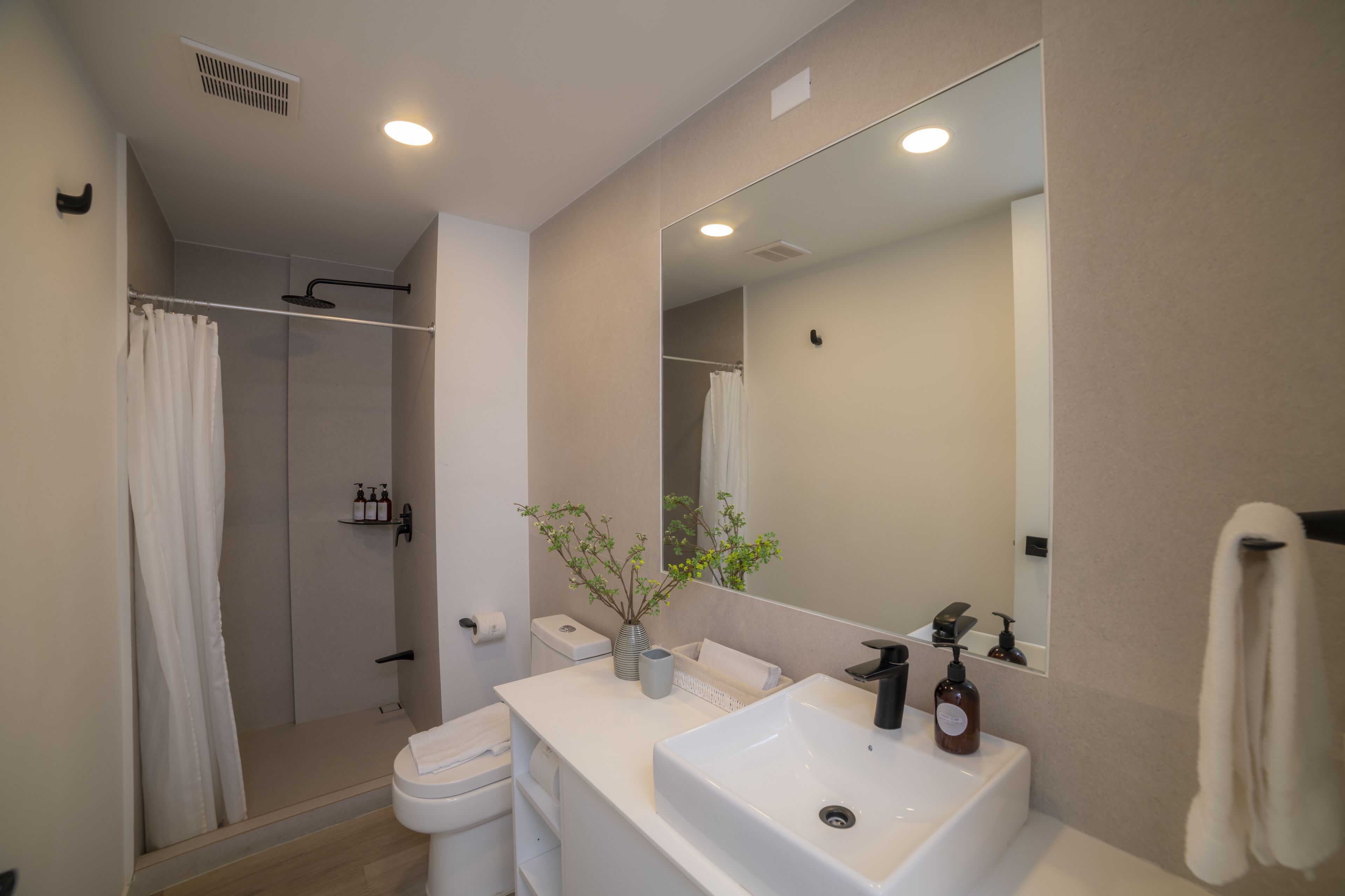 A modern bathroom with a shower, toilet, sink, and large mirror.