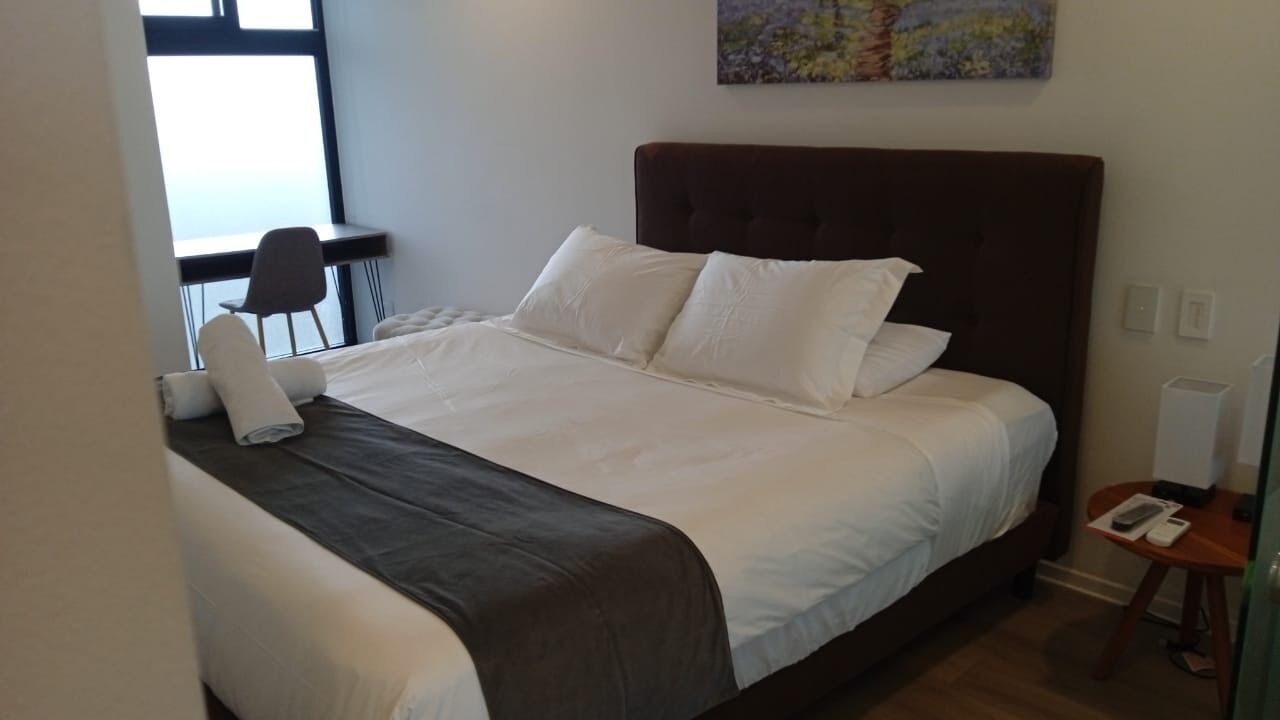 Un lit bien fait, avec du linge de lit blanc et une tête de lit sombre, dans une chambre d’hôtel.
