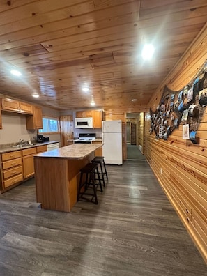 A kitchen with wooden cabinets, a central island with stools, a refrigerator, and a microwave.