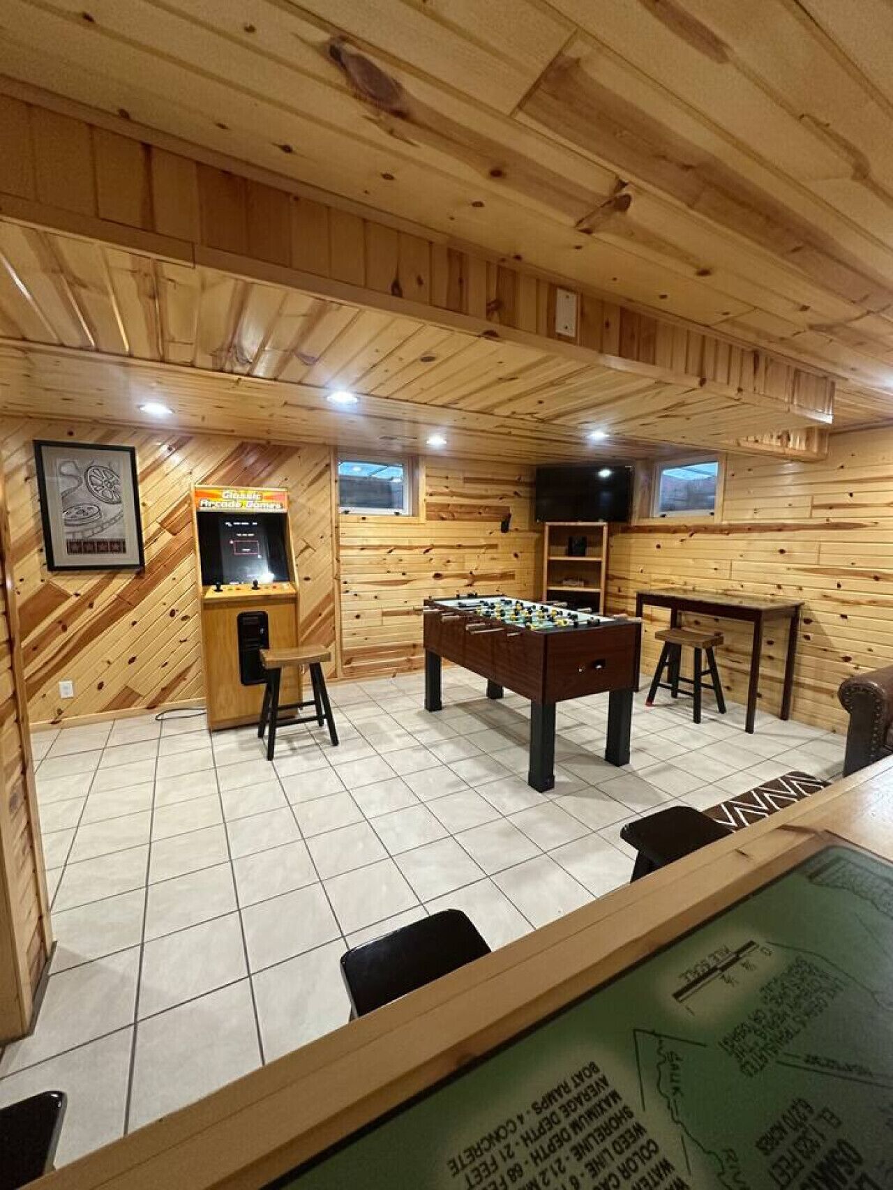 Habitación con paredes y techo de madera, mesa de fútbolín, una pequeña zona de bar y una ventana.