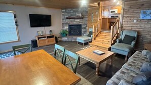 Un intérieur de chalet chaleureux comprenant un coin repas, un salon avec un canapé et une cheminée, ainsi qu’une cuisine.