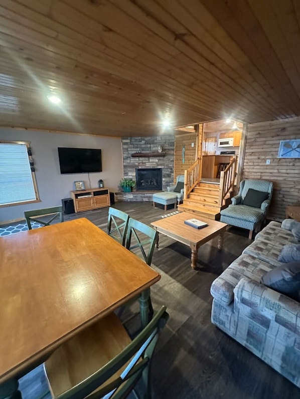 A cozy cabin interior with a dining area, a living room with a sofa and a fireplace, and a kitchen area.