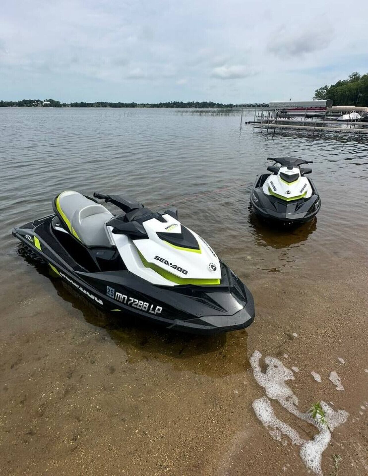 Zwei Sea-400 Jetskis am sandigen Ufer eines ruhigen Gewässers.