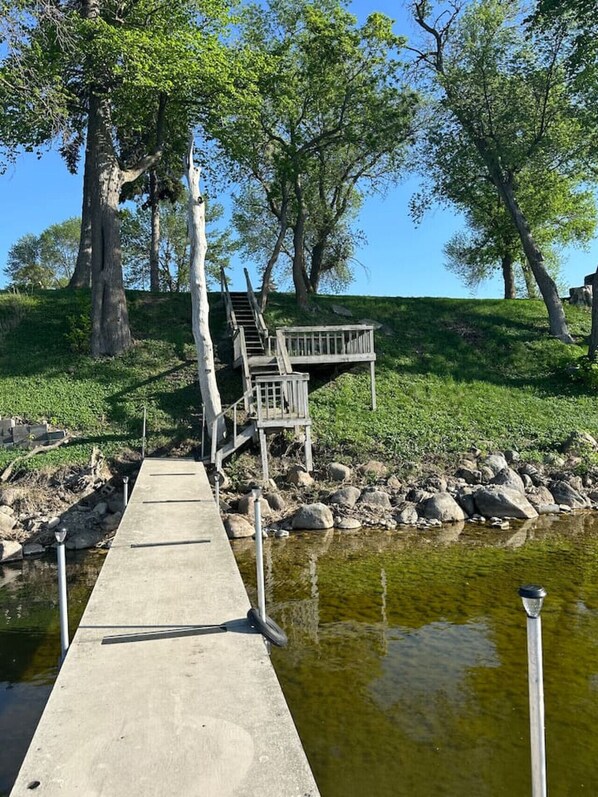 A concrete dock leading to a wooden platform with stairs, surrounded by trees and a calm body of water.