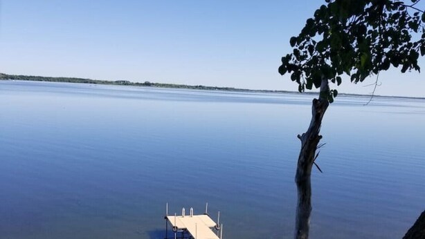 Une jetée en bois s’étendant sur un lac paisible, avec une petite terrasse aménagée comprenant des chaises et une table.