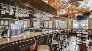Een ruim restaurant met een lange bar, houten plafond en grote ramen.