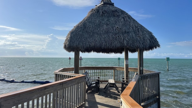 Een houten pier met een rieten gazebo, houten leuningen en een bank.