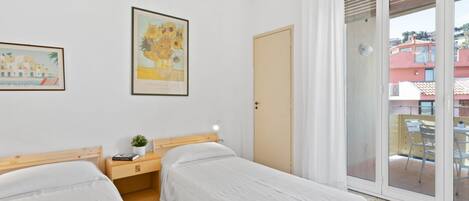 Una habitación con dos camas, una mesita de noche con lámpara, un cuadro en la pared y un ventanal corredero que da a un espacio exterior.