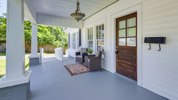 A covered porch with a white railing, a wooden door, and a hanging light fixture.