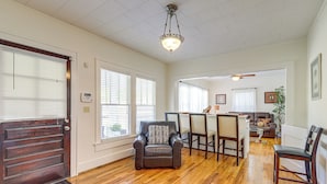 A spacious living room with hardwood flooring, a dark brown leather armchair, a dining area with a table and chairs, and a ceiling fan.