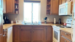 A kitchen with wooden cabinets, a microwave, a stove, and a sink. - Warm and Bright in the Heart of Downtown Friday Harbor (Friday Harbor)