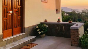 Una casa con puerta de madera, un balcón pequeño con plantas en macetas y vistas al paisaje.