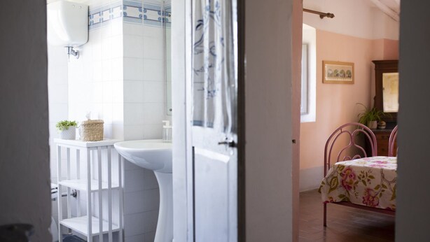 Ein Badezimmer mit Waschbecken, Toilette und Regal, alles in Weiß. Ein Korb mit Pflanze ist ebenfalls vorhanden.