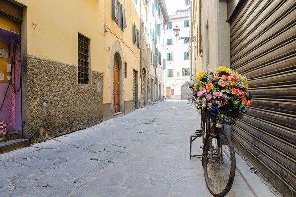 A narrow street with a bicycle parked on the right, a closed shop with a shutter, and a building with a stone facade.