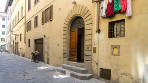 A narrow street with a building featuring a wooden door, stone steps, and laundry hanging outside.