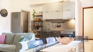 A modern kitchen with white cabinets, a stainless steel refrigerator, a glass dining table, and a decorative bowl.