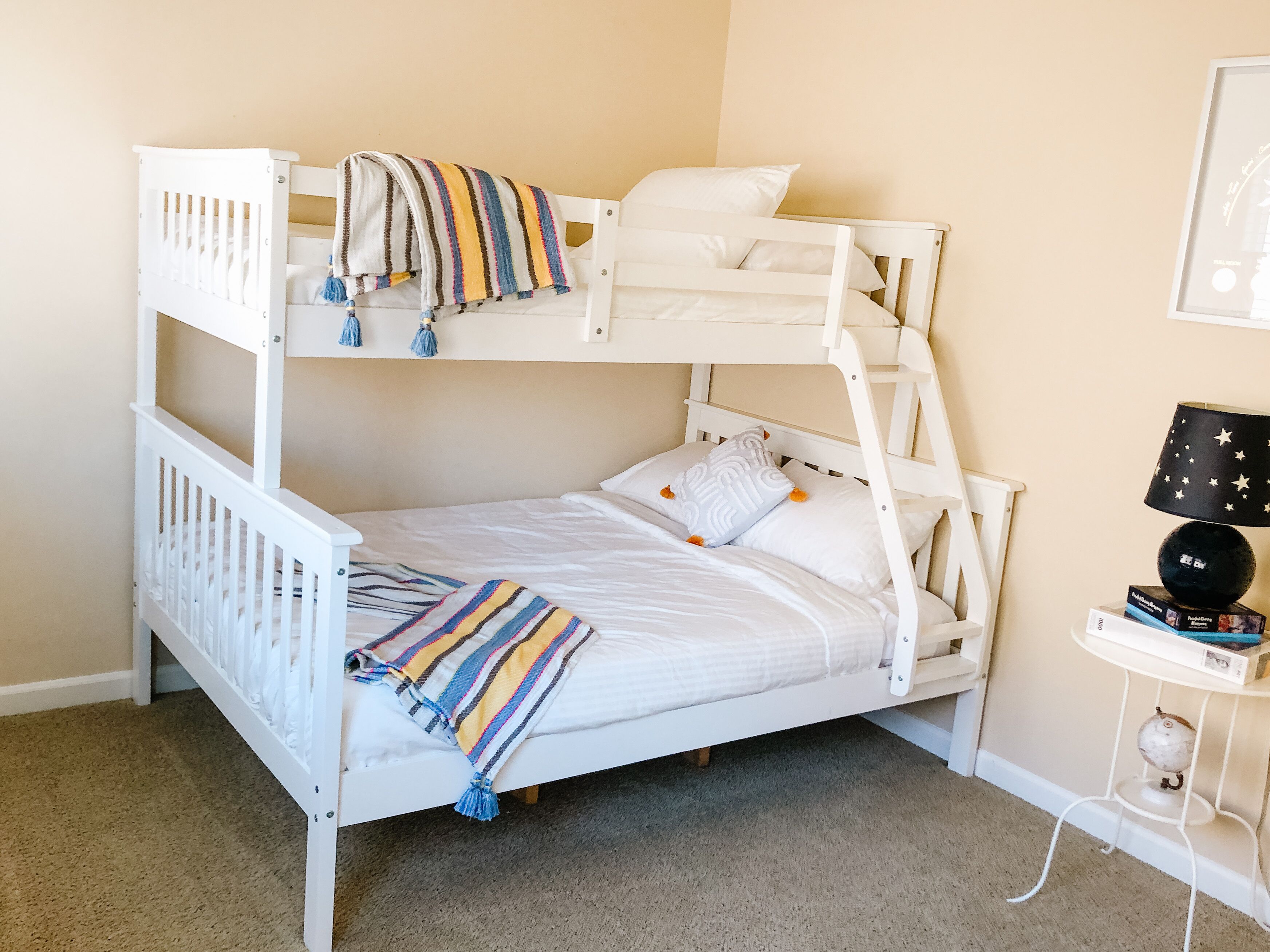 A bunk bed with a striped blanket and pillows, a small table with a lamp, and a globe.