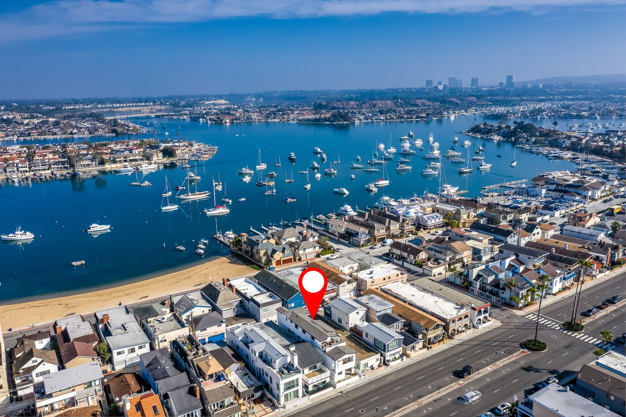An aerial view of a coastal town with a marina filled with boats, a beach, and a mix of residential and commercial buildings.