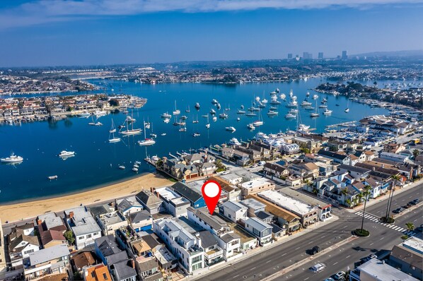 An aerial view of a coastal town with a marina filled with boats, a beach, and a mix of residential and commercial buildings.